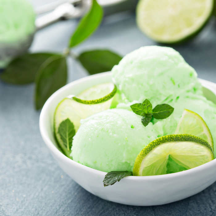 Freshly churned pastel green key lime gelato displayed in a stainless steel ice cream pan topped with fresh lime slices.