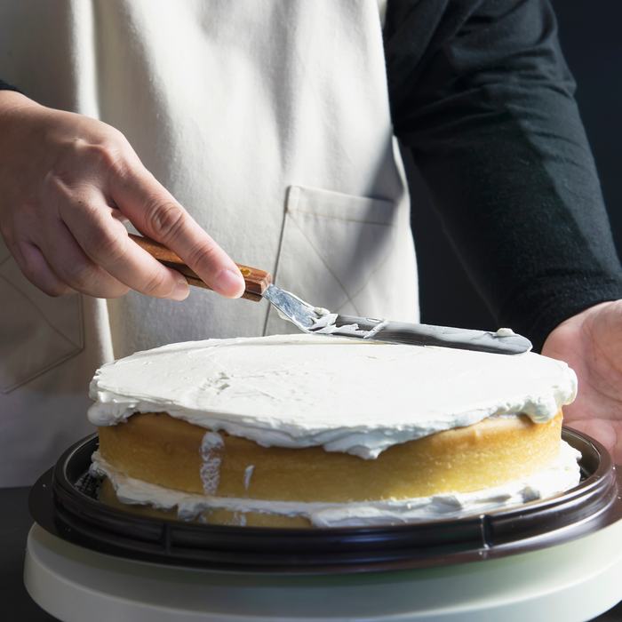 Professional baker spreading smooth 50Express white buttercream icing onto a layered cake