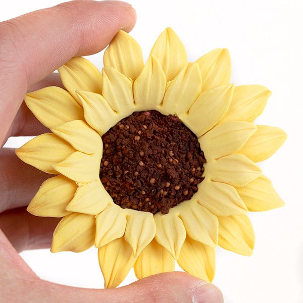 Close-up of delicate yellow gumpaste sunflower petals and dark brown seed center for rustic wedding cake decorating.