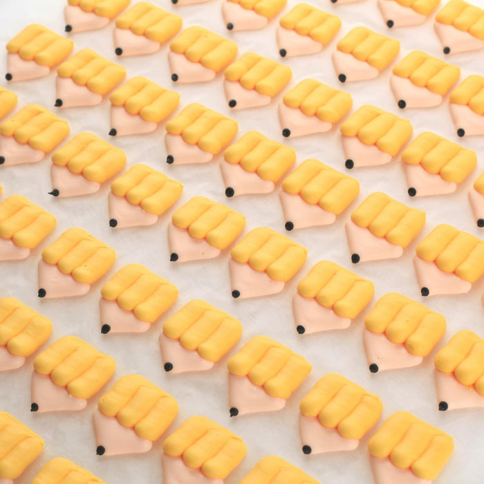 Pre-made edible royal icing book and crayon toppers applied to baked cookies and chocolates for efficient, high-volume bakery decorating by Caljava