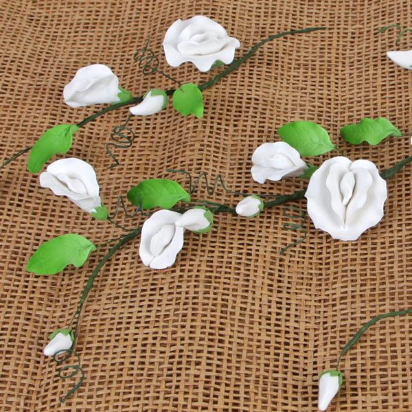 Detailed close-up of handmade white gumpaste sweet pea buds and green leaves wired for wedding cake design.